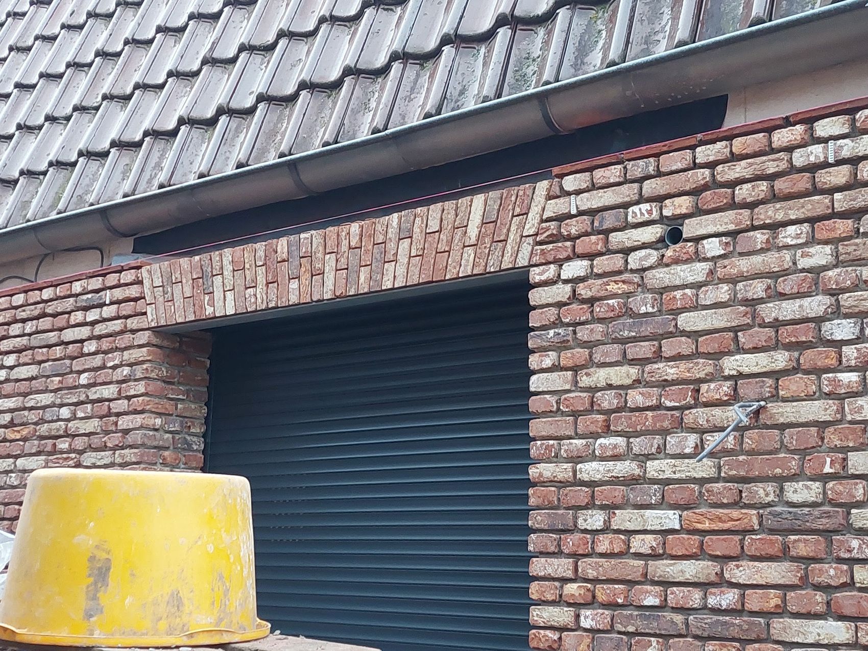 Nieuw metselwerk in rode en bruine stenen rond een zwarte garagedeur