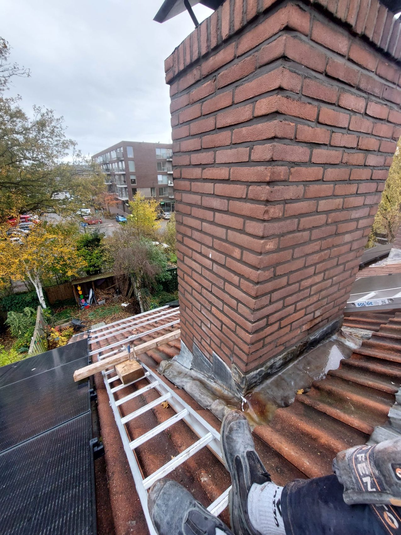 Een hoge bakstenen schoorsteen met nieuw lood op een pannendak
