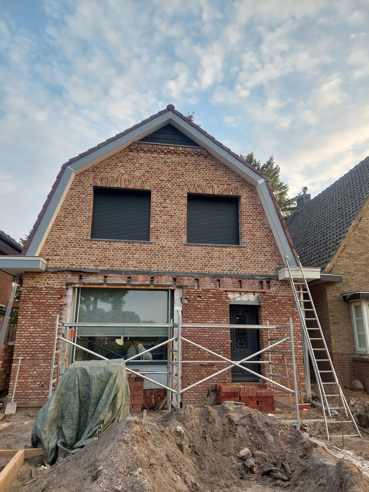 Een woning met een nieuwe bakstenen voorgevel tijdens de verbouwing, met steigers en een ladder