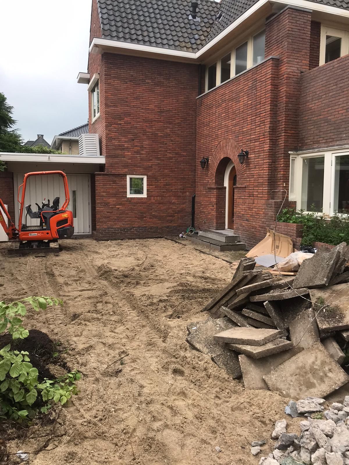 Grondwerk met een minigraver naast een grote bakstenen woning